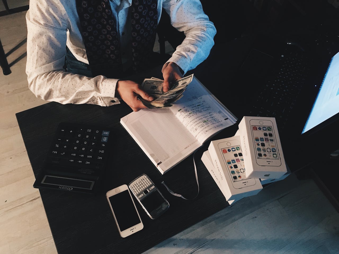 portfolio-03 Businessman organizing finances with tech devices and cash on desk.