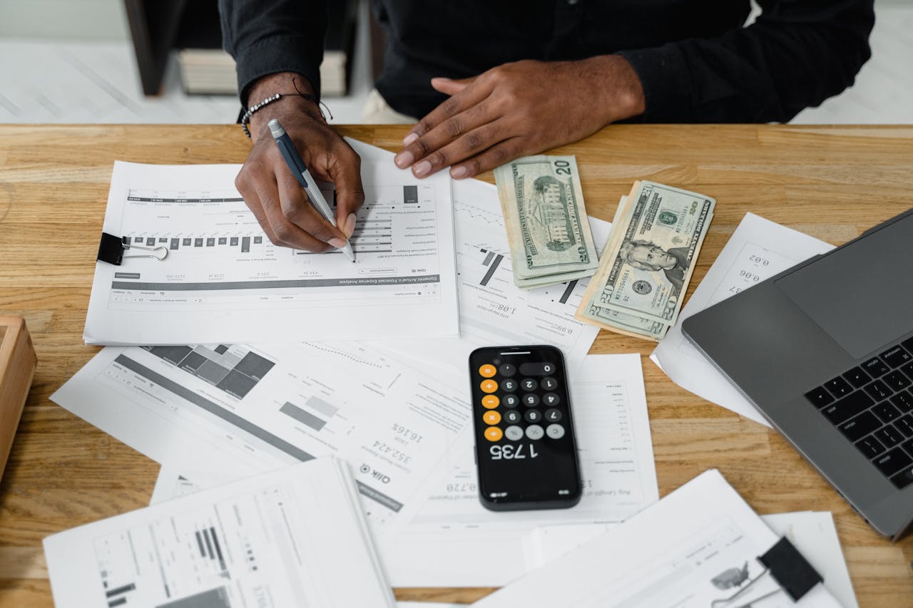 portfolio-04 Man working on financial reports with calculator, money, and laptop on a desk.